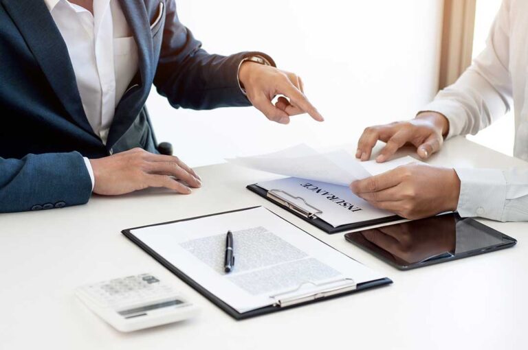 Freelancer reviewing insurance documents beside a laptop, camera equipment, and organized business records.